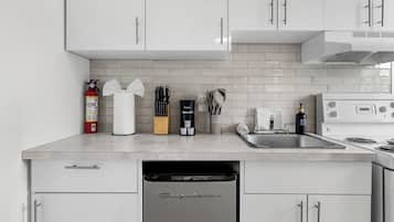 A modern kitchen with white cabinets, a dishwasher, a sink, and a stove.