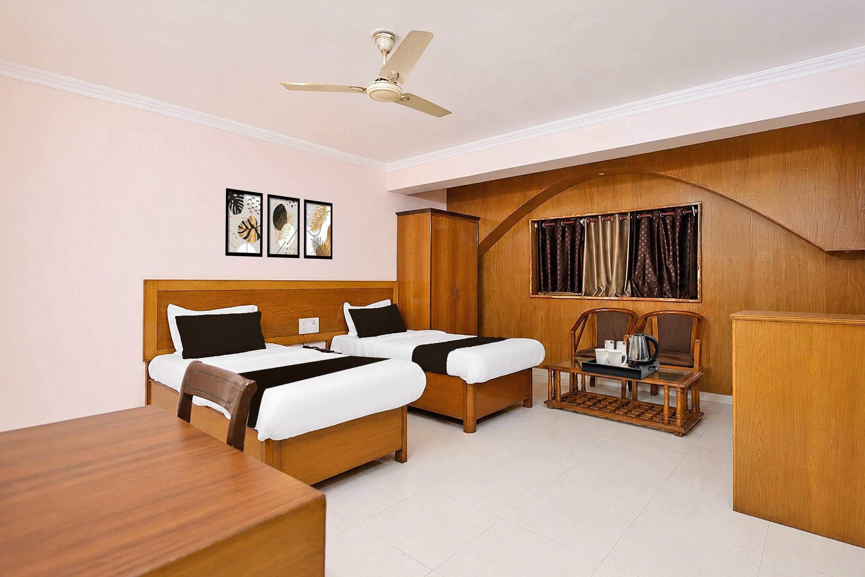 Une chambre d’hôtel avec deux lits, un bureau en bois, une table basse et un ventilateur de plafond.