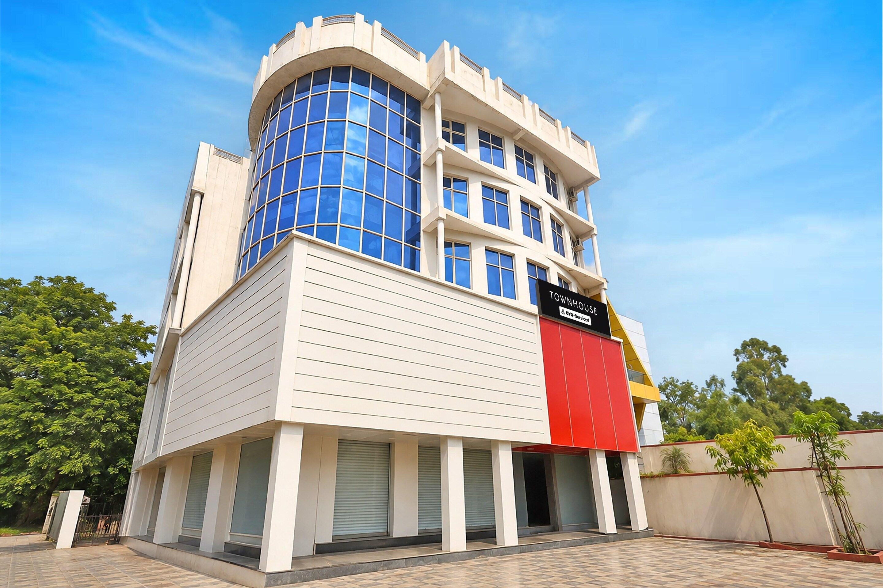 Un immeuble à plusieurs étages doté d’une façade en verre bleue très visible et d’une enseigne rouge et blanche indiquant qu’il s’agit d’une maison de ville.