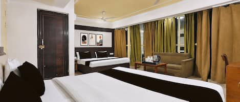 A hotel room with a bed, a sofa, a table with a coffee maker, and a ceiling fan.
