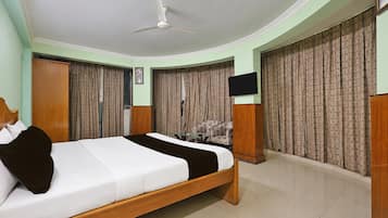 A bedroom with a bed, a ceiling fan, a TV, and curtains.