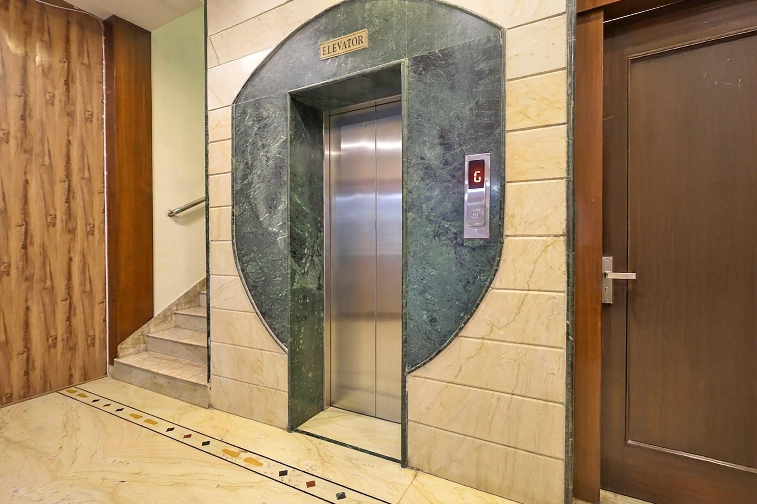 An elevator with a digital display, a sign above it, and a wooden door to the right.