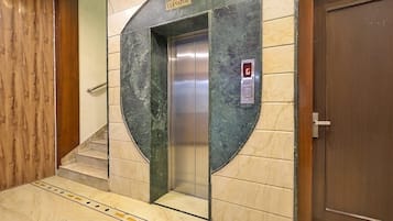 An elevator with a digital display, a sign above it, and a wooden door to the right.
