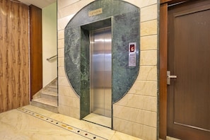 Un ascensor con una pantalla digital, un cartel encima y una puerta de madera a la derecha.