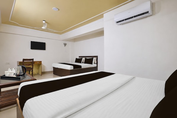 Una habitación de hotel con cama, escritorio con silla, cafetera y equipo de aire acondicionado.