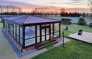 A glass-enclosed building with a tiled roof, a wooden deck, and a grassy yard. - Awesome home in Darlowo with sauna (Darlowo)