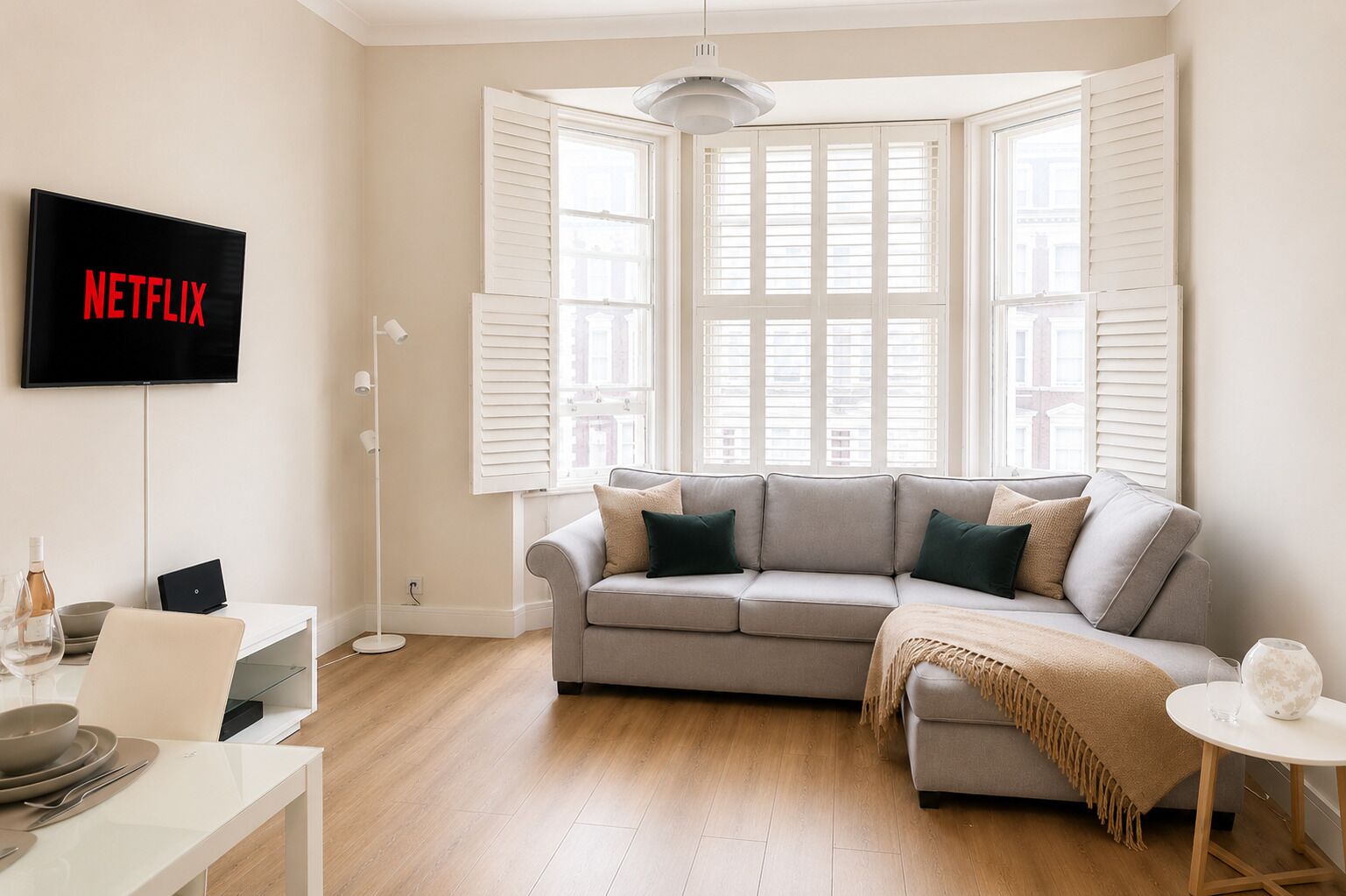 A modern living room with a grey sofa, a flat-screen TV mounted on the wall, and a dining area with a white table and chairs.