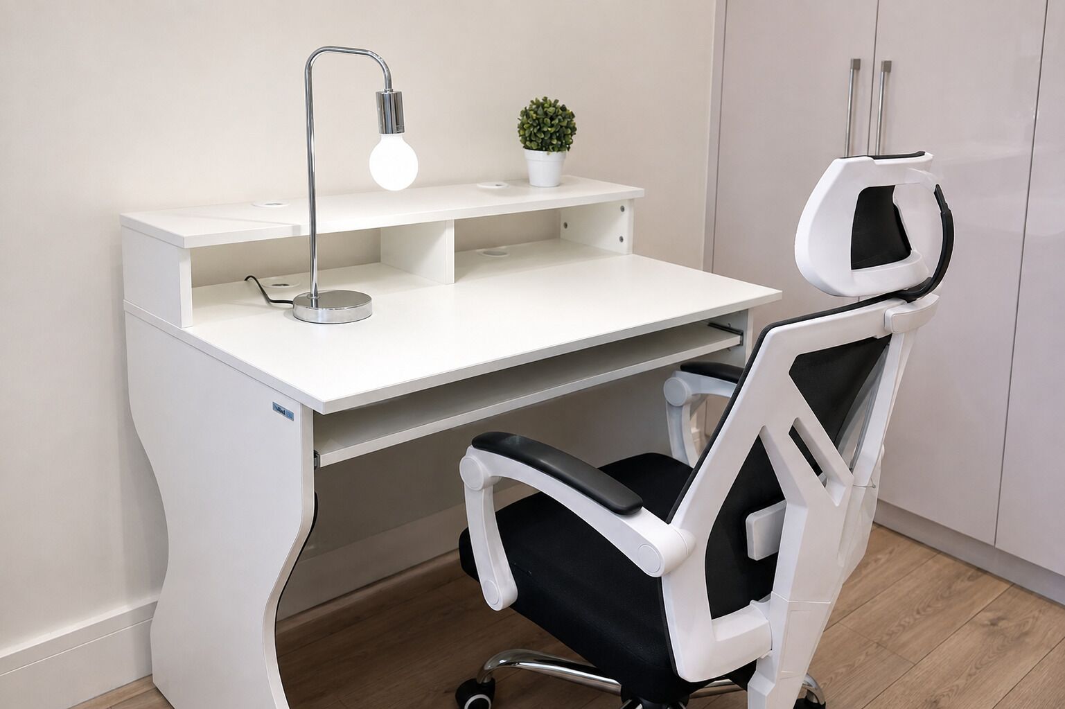 A white desk with a lamp, a potted plant, and a modern office chair.