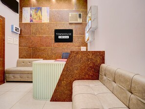 A reception area with a sign indicating it is serviced by OYO. There is a reception desk, a sofa, and a wall with artwork.