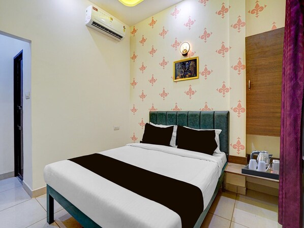 A hotel room with a bed, a bedside table, a wardrobe, and an air conditioning unit.