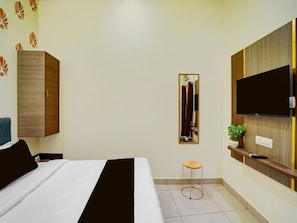 A hotel room with a bed, a wardrobe, a television, a mirror, a small stool, and a potted plant. - Deluxe Room Parth Residency (Varanasi)