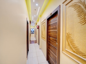A hotel hallway with a tiled floor, wooden doors, and a fire extinguisher on the wall.
