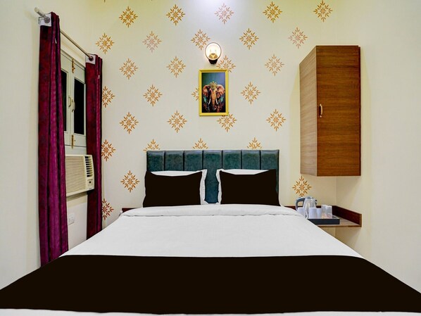 A hotel room with a bed, a nightstand, a wardrobe, a wall with a decorative pattern, and a window with curtains.