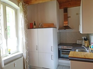 Cuina amb armaris blancs, fornet, rentapeus i finestra amb cortines.