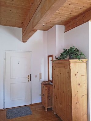 Ein Zimmer mit Holzboden, einer weißen Tür, einem Holzschrank mit Spiegel und einer Topfpflanze.