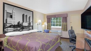 A hotel room with a large bed, a desk with a chair, a television, and a window with curtains.