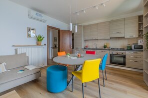 A modern kitchen with wooden cabinets, a dining table with colorful chairs, and a built-in oven. - Viandante Lake View in Bellano (Bellano)