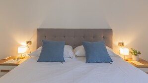 Een bed met een gestoffeerd hoofdbord, twee bedlampjes en een nachtkastje met een plant.
