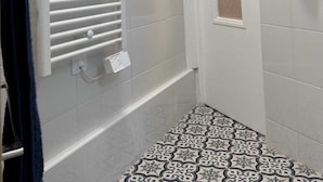A bathroom with a white tiled wall, a shower with a white glass door, a towel rack with a dark towel, and patterned floor tiles. - Charming Apartment 1br/6p - Deauville (Deauville)