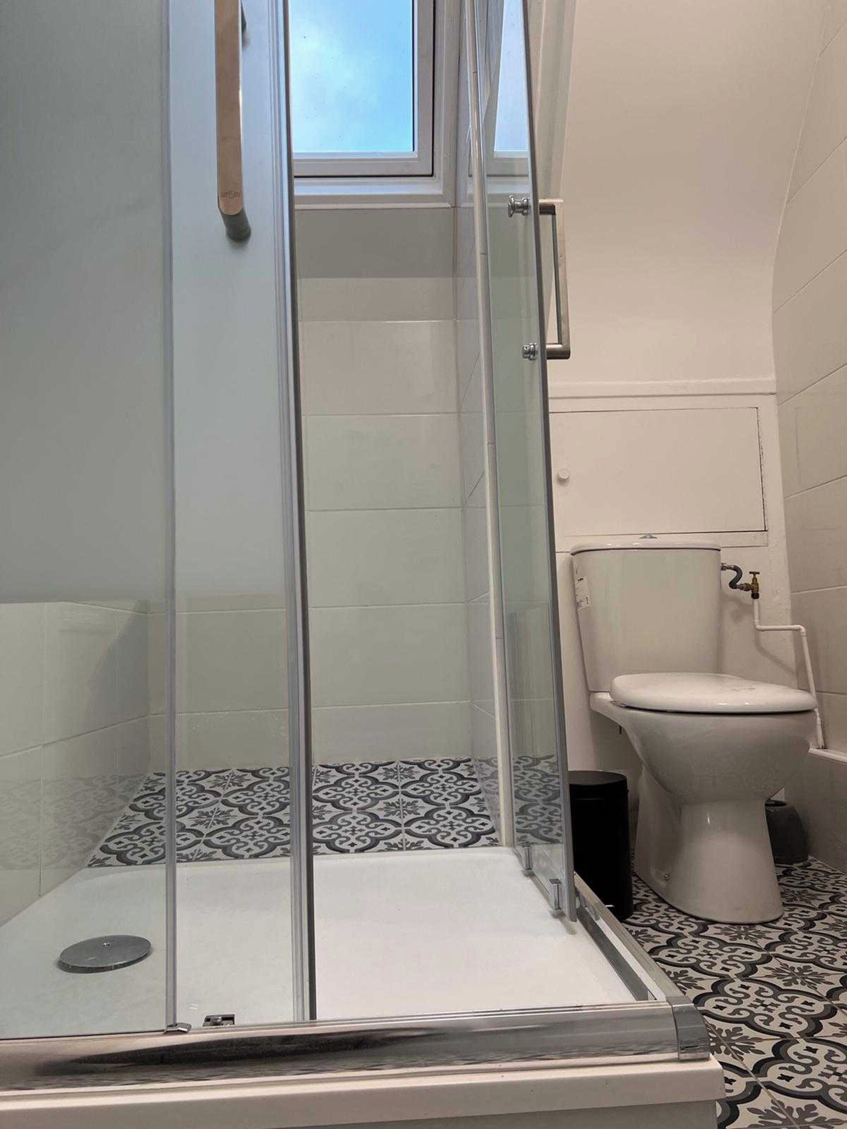 A bathroom with a glass-enclosed shower, a toilet, and patterned floor tiles.