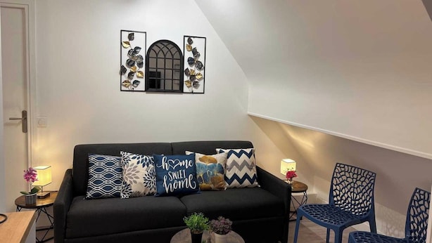 A modern living room with a black sofa, decorative pillows, a small round table with plants, and blue chairs. - Charming Apartment 1br/6p - Deauville (Deauville)