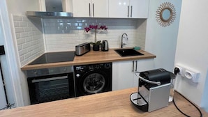 A compact kitchen with white cabinets, a stainless steel range hood, a washing machine, a toaster, and a coffee maker. - Charming Apartment 1br/6p - Deauville (Deauville)