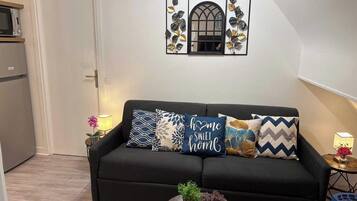A living room with a dark sofa, decorative pillows, a small round table with plants, and a wall-mounted mirror with a floral design.