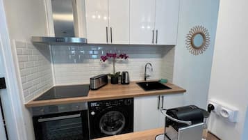 A compact kitchen with white cabinets, a stainless steel range hood, a washing machine, a toaster, and a coffee maker.