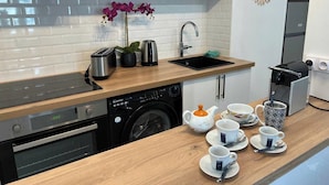 A modern kitchen with a dishwasher, oven, sink, and a coffee station with cups and a teapot. - Charming Apartment 1br/6p - Deauville (Deauville)