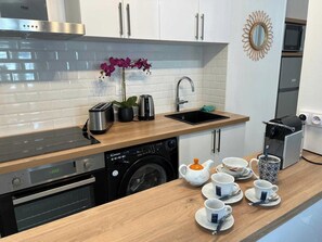 Eine moderne Küche mit Geschirrspüler, Backofen, Spüle und einer Kaffeestation inklusive Tassen und Teekanne.