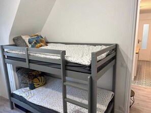 A bunk bed with a lower bunk, a pillow with a leaf pattern, and a door in the background. - Charming Apartment 1br/6p - Deauville (Deauville)