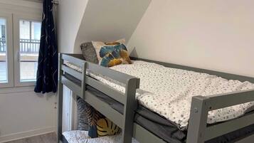 A small, single-bedded room with a sloped ceiling, a window with curtains, and a view of the outside.