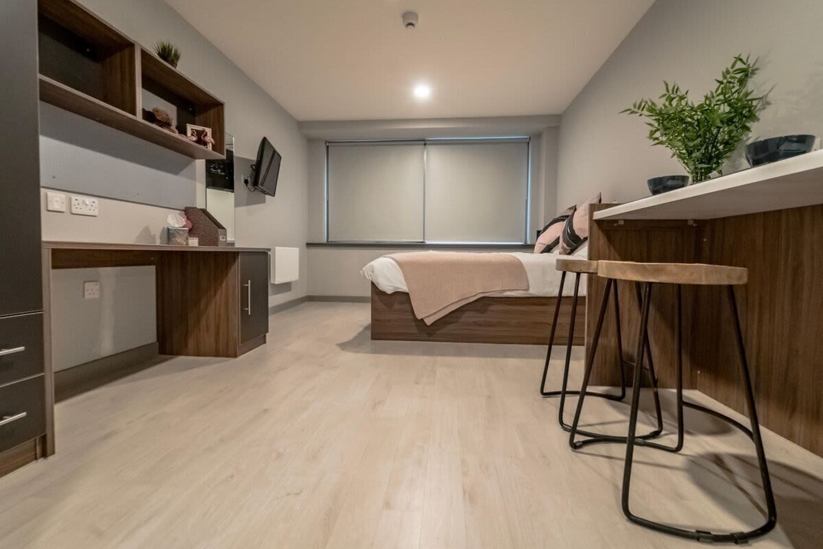 A compact bedroom with a bed, bedside table, and a small kitchenette area.