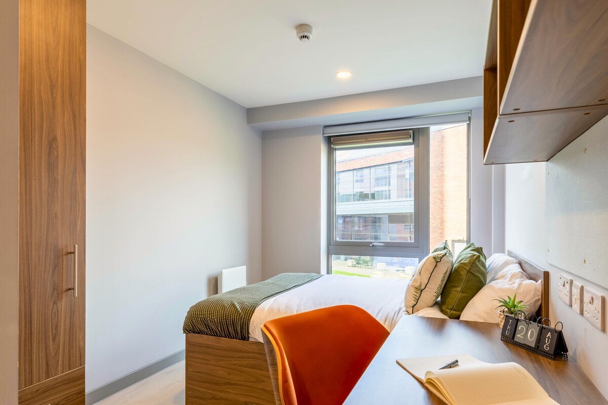 A modern bedroom with a bed, a desk, and a window.
