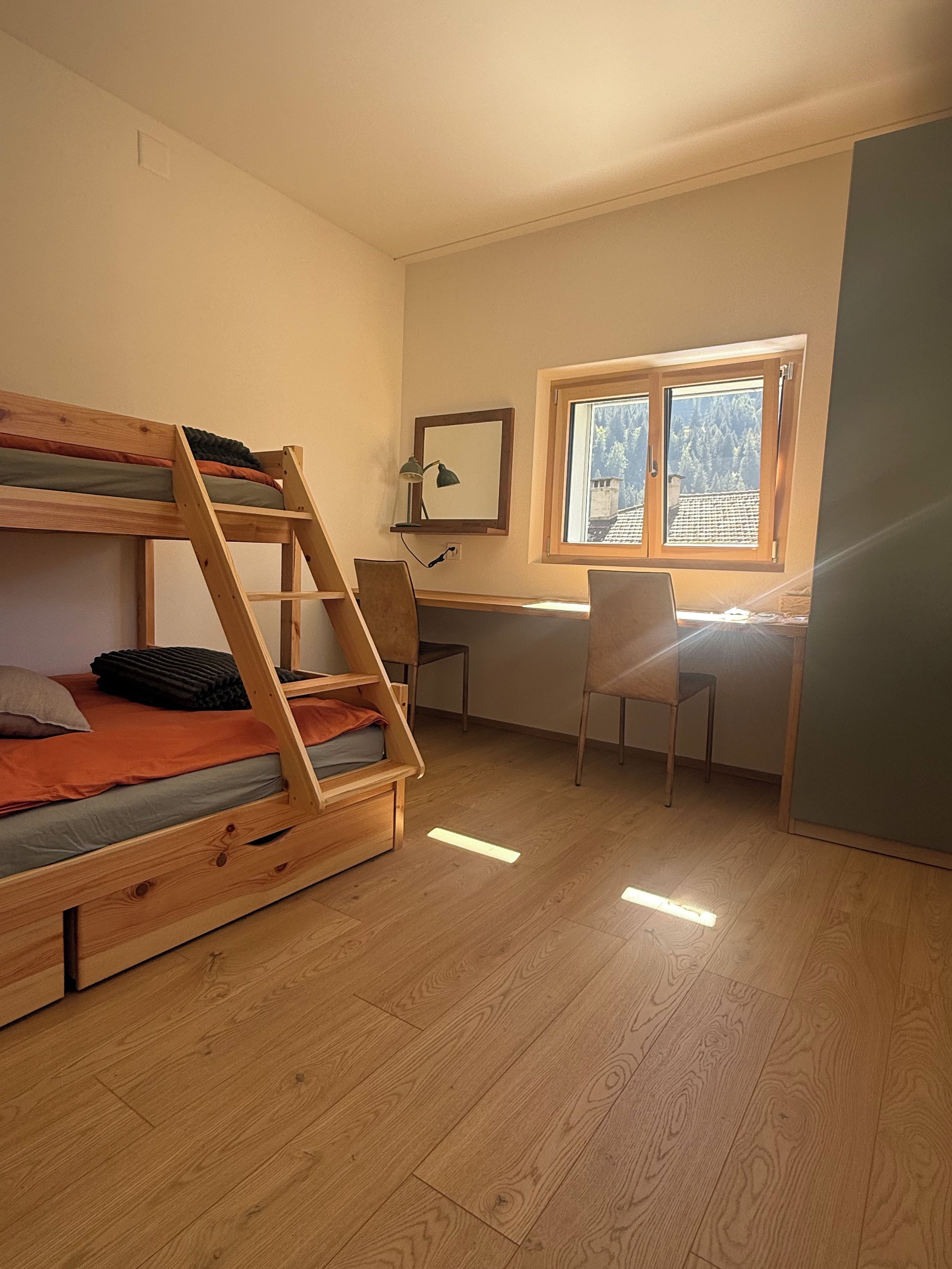 Une chambre avec un lit superposé, un bureau, une chaise et une fenêtre donnant sur des arbres.