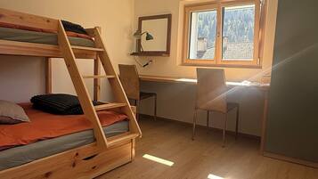 Ein Zimmer mit Etagenbett, Schreibtisch, Stuhl und einem Fenster mit Blick auf Bäume.