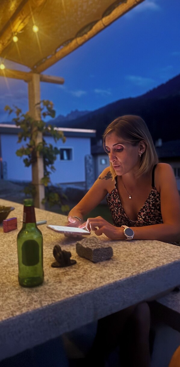 A person sitting at an outdoor table with a bottle and a tablet.