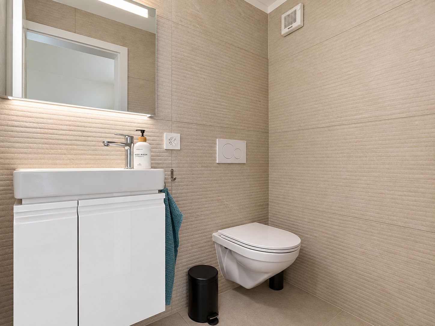 A bathroom with a white sink, a mirror, a toilet, and a trash bin.