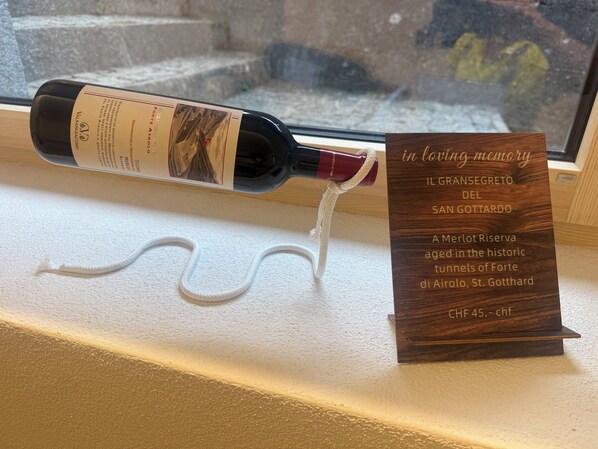 Une bouteille de vin avec une étiquette, une enseigne en bois avec du texte, et une corde blanche posée sur un rebord de fenêtre.