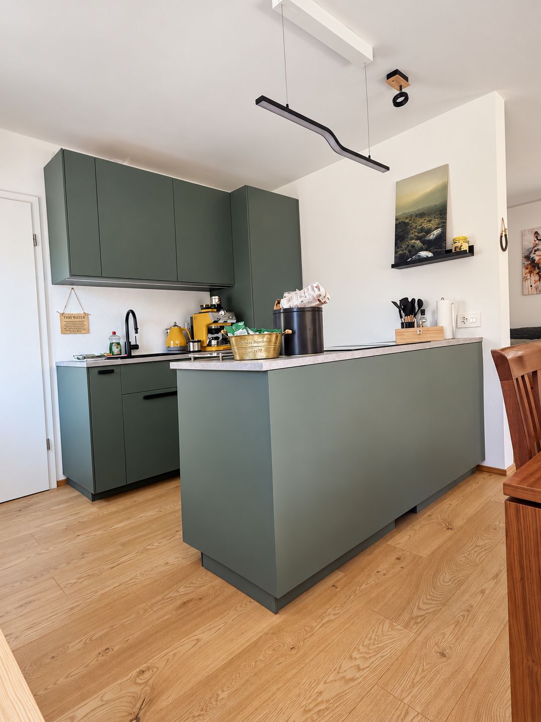 Een moderne keuken met een centraal eiland, groene kastjes en een houten vloer.