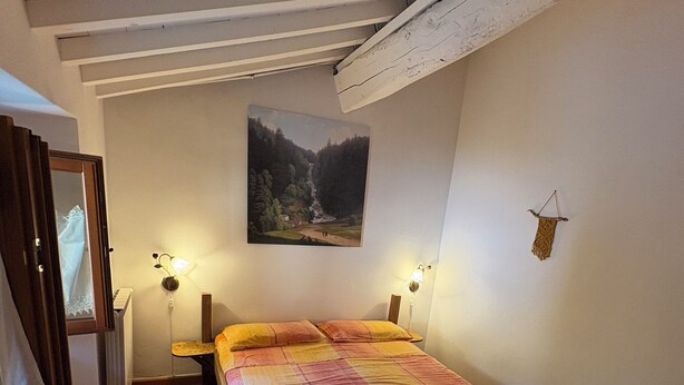 Un dormitorio con cama, dos lámparas de noche, un cuadro en la pared y cabecera de madera.