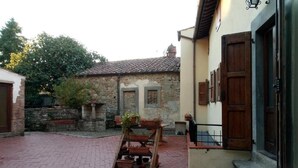 Un patio con piso de ladrillo, un banco de madera y una jardinera en la pared con plantas.