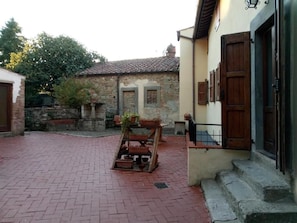 Un patio con piso de ladrillo, un banco de madera y una jardinera en la pared con plantas.