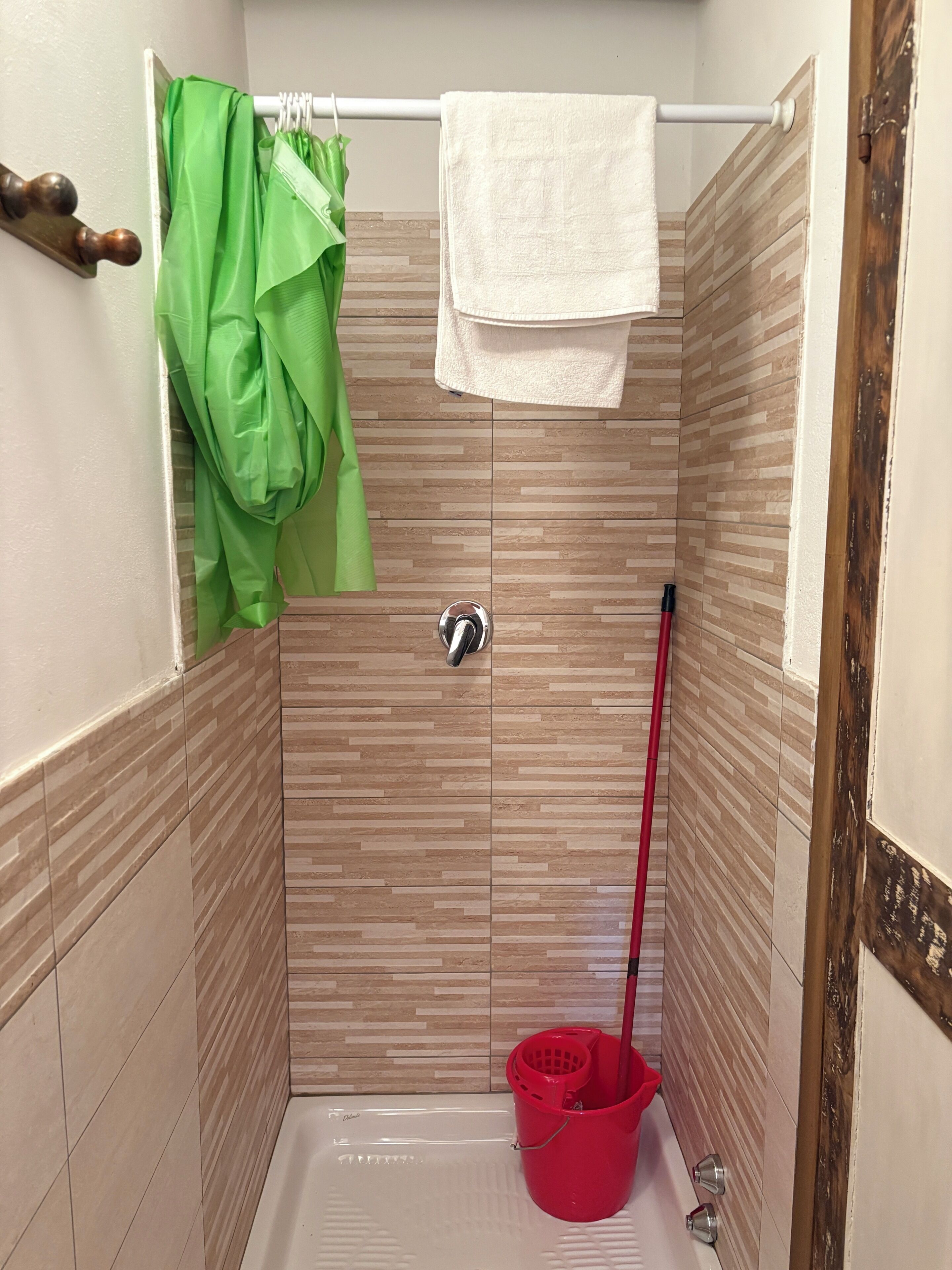Une cabine de douche avec un porte-serviettes, une serviette verte, un seau rouge et une pomme de douche.