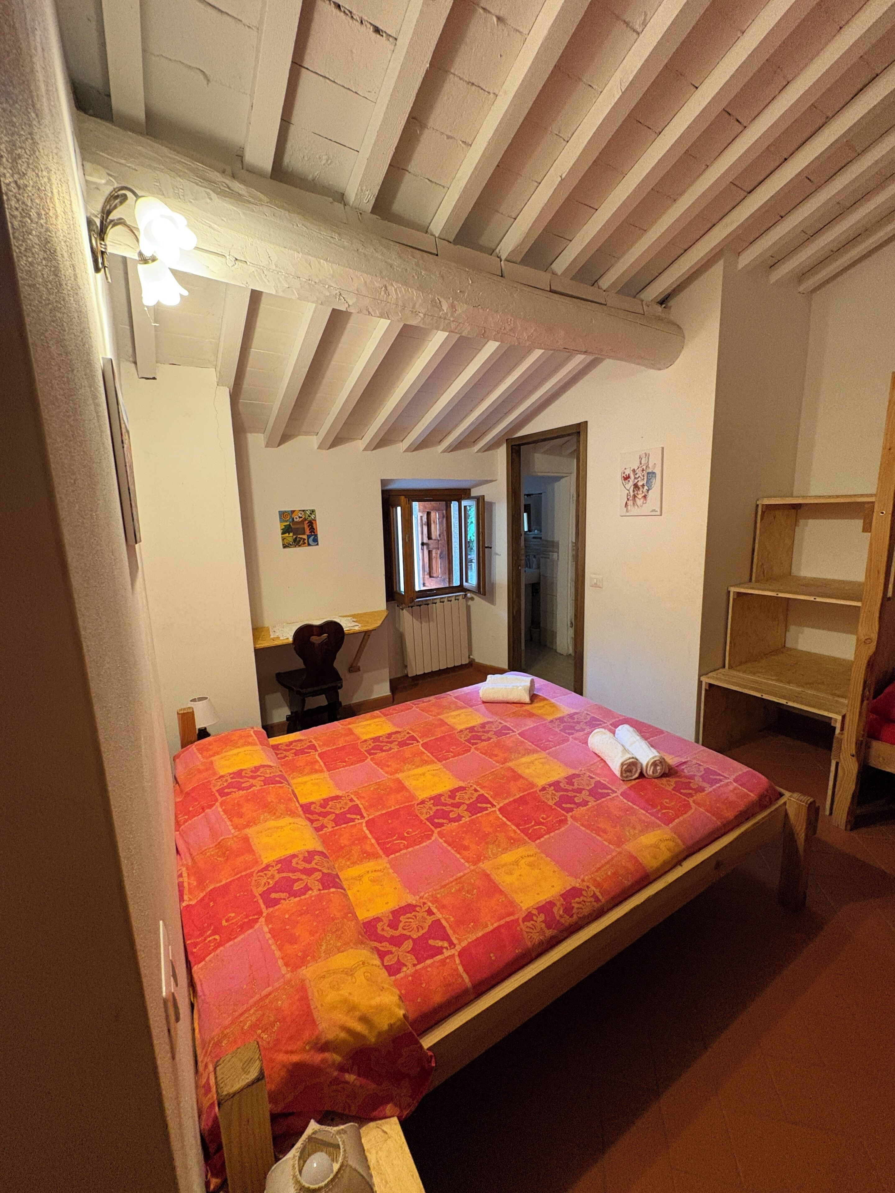 Una habitación con una cama, un escritorio, una silla y un estante de madera.
