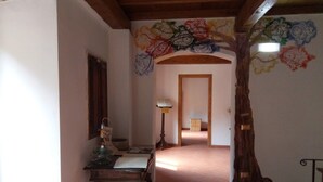 Un pasillo con una escalera de madera, un escritorio con lámpara y un muro con motivos florales coloridos.