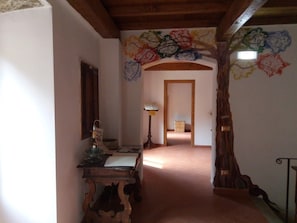Un pasillo con una escalera de madera, un escritorio con lámpara y un muro con motivos florales coloridos.