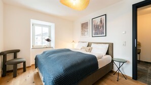 A bedroom with a bed, a window, a chair, a bedside table, and a hanging light fixture. - Hochkalter Vacation Rental (Schönau am Königssee)