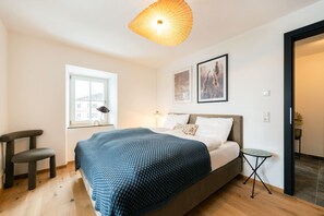 Ein Schlafzimmer mit Bett, Fenster, Stuhl, Nachttisch und einer Pendelleuchte.