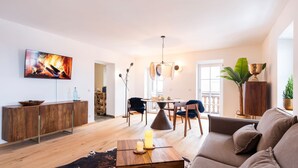 A modern living room with a flat-screen TV, wooden furniture, a dining area, and a large window. - Hochkalter Vacation Rental (Schönau am Königssee)